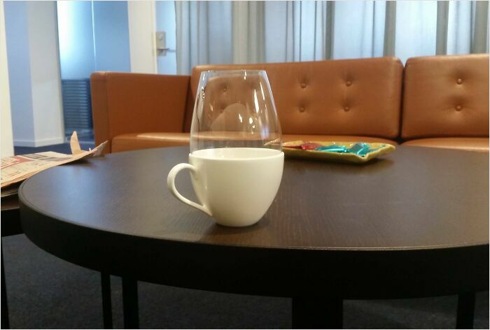 A coffee mug perfectly fits inside a wine glass on a table in front of a brown sofa, illustrating a satisfying perfect fit.