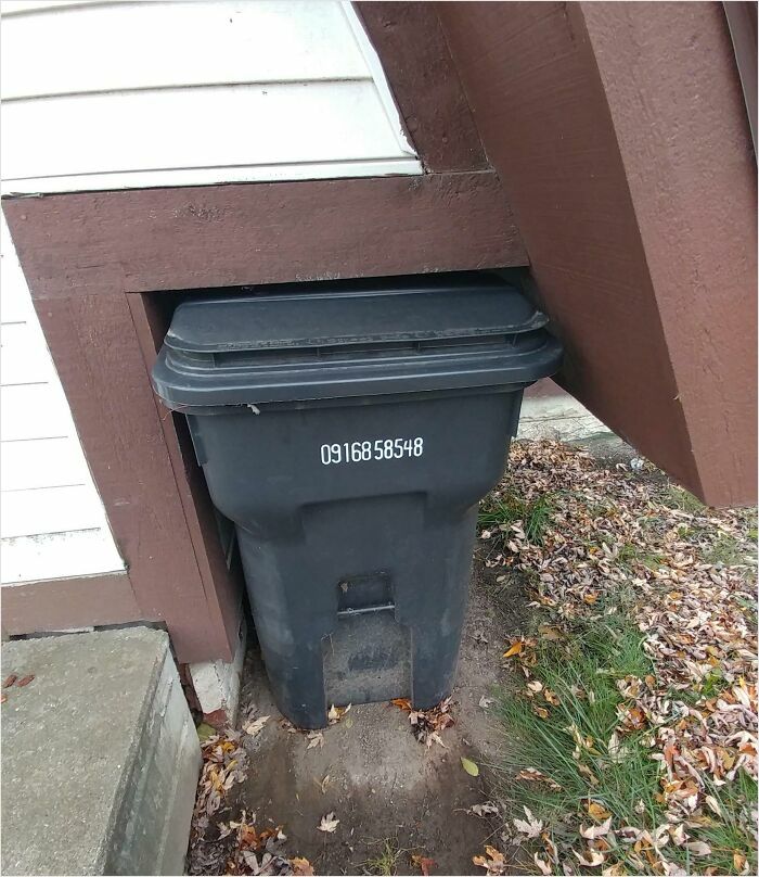 A garbage bin perfectly fits into a narrow space under a roof overhang, demonstrating a satisfying perfect fit.