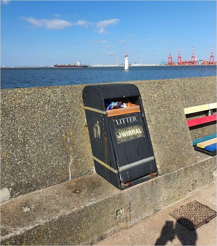 Litter bin perfectly fitted into stone wall by the seaside under a blue sky.