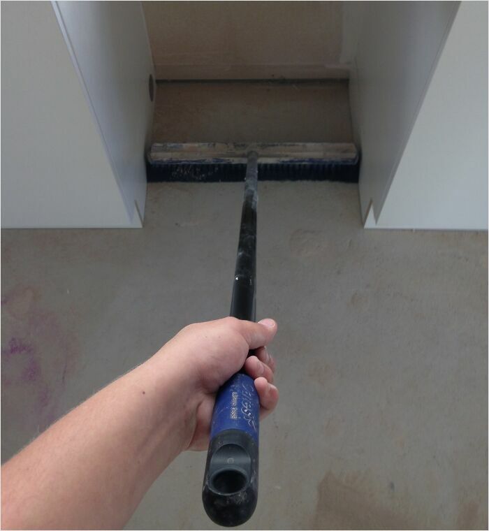 Hand holding a broom fitting perfectly between two cabinets, showcasing a satisfying perfect fit.