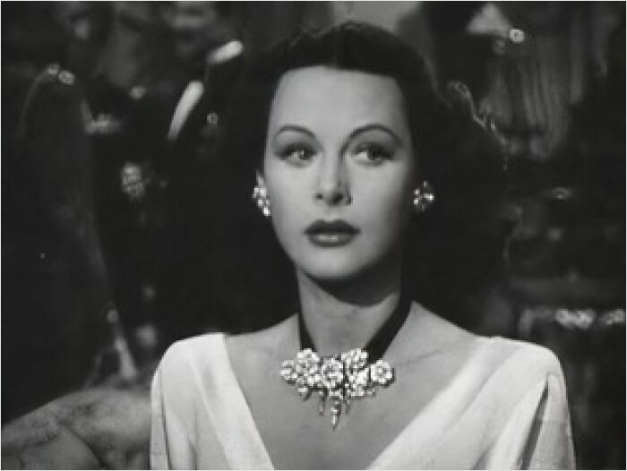 A woman with a classic hairstyle and elegant jewelry in a vintage black and white photo.