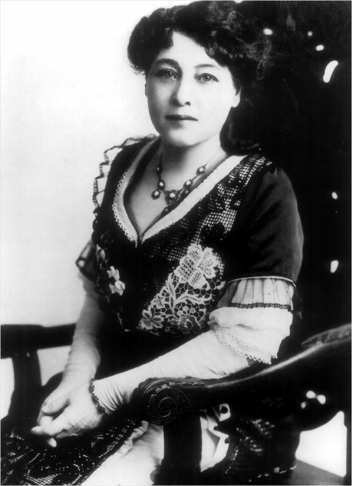 A woman in early 20th-century attire, seated with hands folded, influential moment in history.