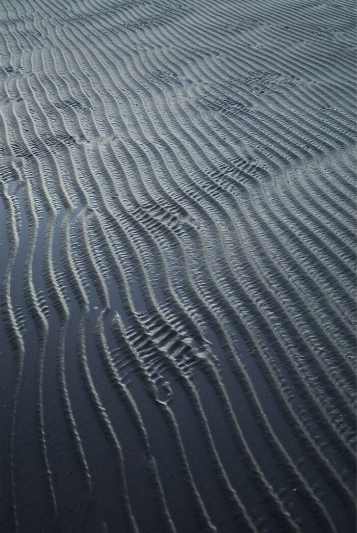 Ocean waves captured in fascinating patterns on a sandy beach at low tide.