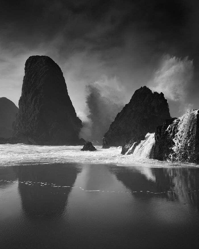 Monochrome photograph capturing waves crashing against large rock formations.