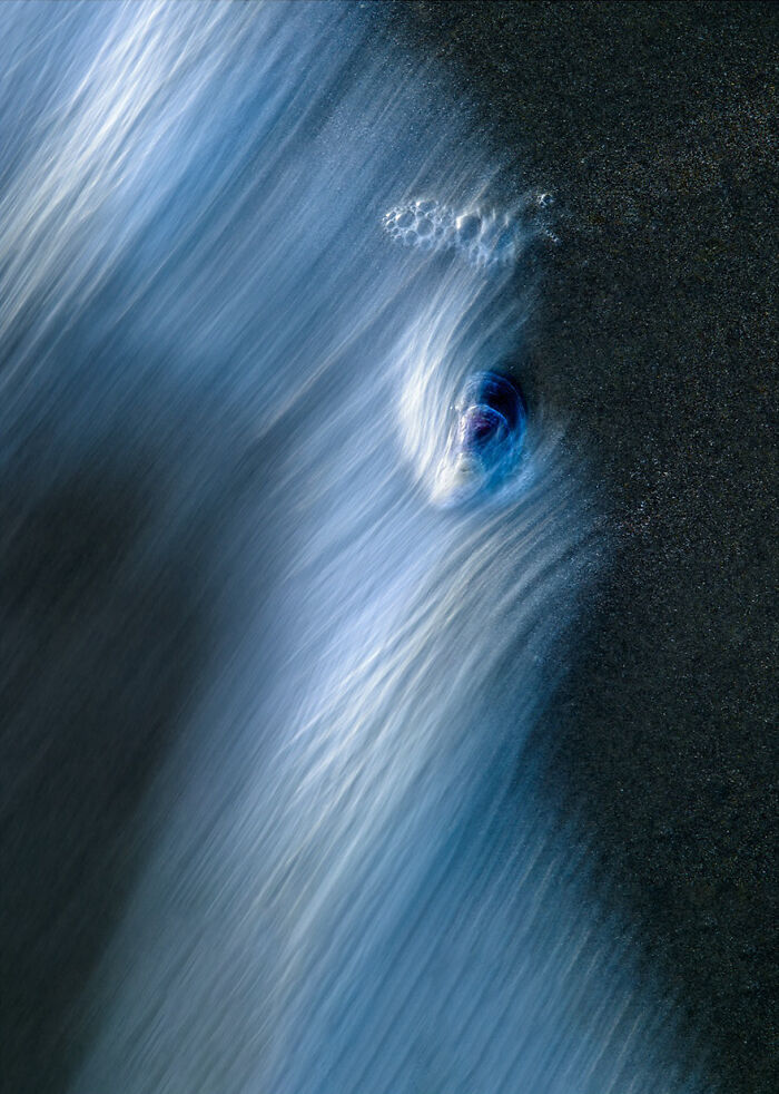 Abstract wave photography showcasing a mesmerizing flow of water over sand, with bubbles accentuating the blue and white hues.