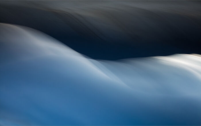 Abstract waves captured by photographer, showcasing smooth, flowing motion and blending blue hues.