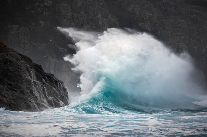 Dynamic photo capturing a powerful wave crashing against rocky cliffs.