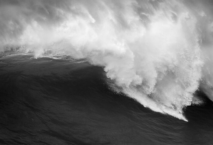 Black and white photo of a large, crashing ocean wave captured by a photographer.