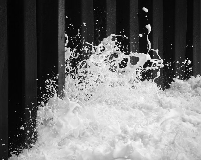 Black and white photo capturing waves splashing against a dark background, creating a dramatic and fascinating effect.