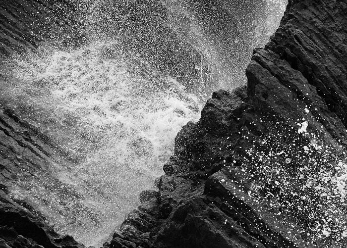 Black and white photo capturing waves crashing against jagged rocks.