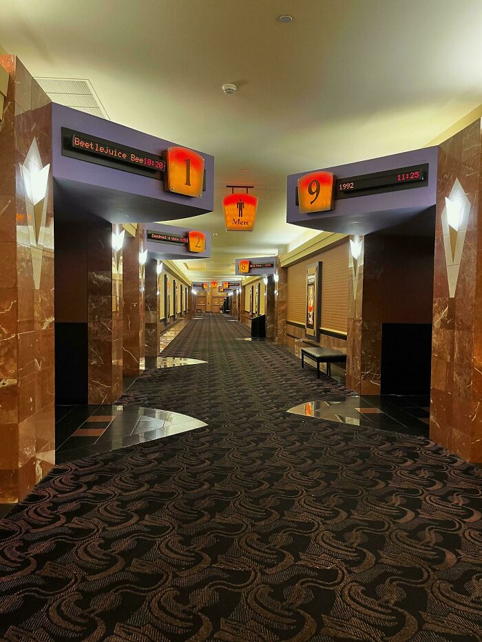 A theater hallway resembling videogame graphics, with patterned carpet and movie signs overhead.