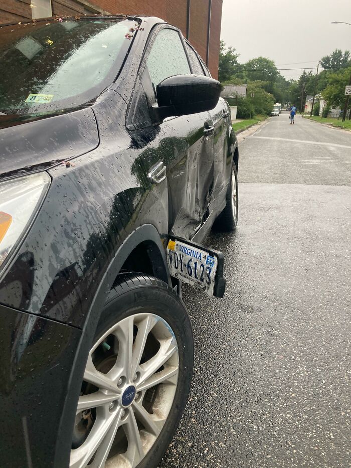 Damaged car with bent license plate in rainy street, illustrating idiots in cars.