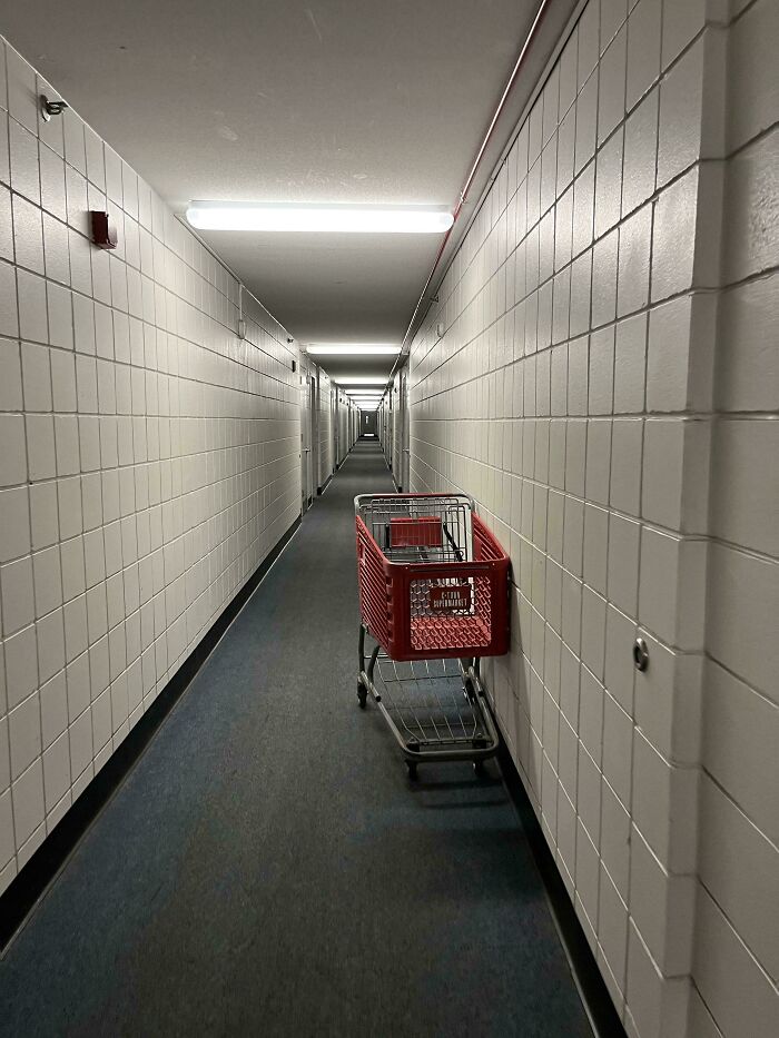 Narrow white corridor with a red shopping cart, resembling a scene from videogames.