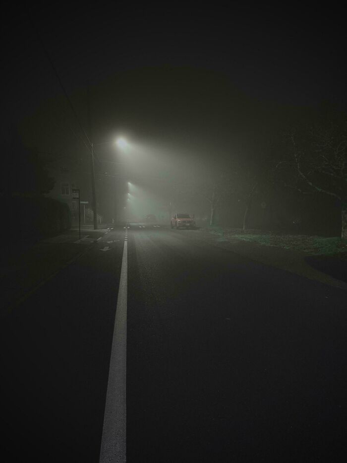 Foggy street at night with streetlights casting a glow, resembling a scene from a video game.