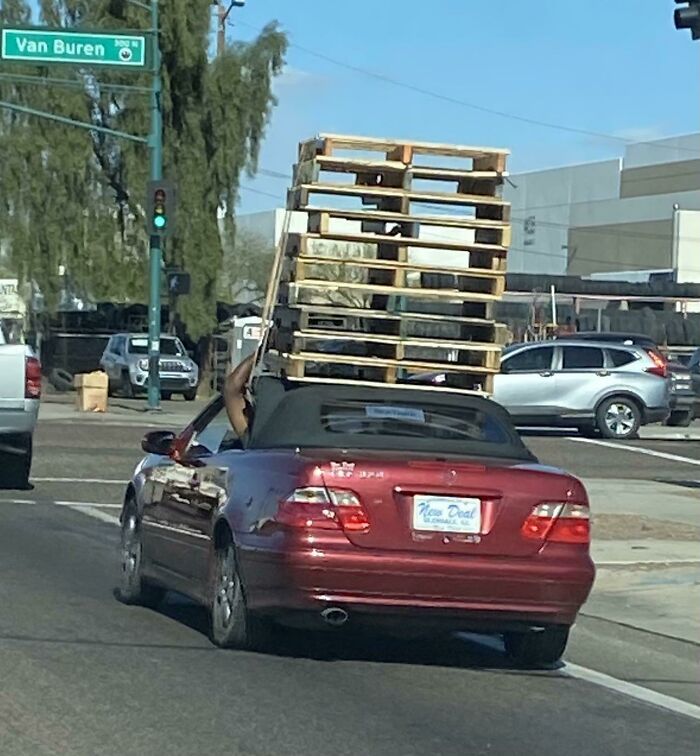 Convertible car carrying a towering stack of wooden pallets on top, illustrating an unsafe driving scenario.