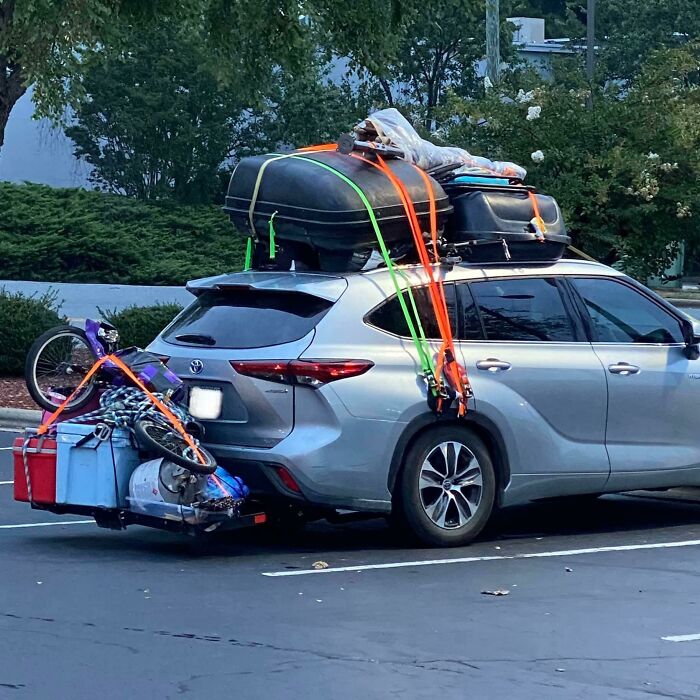 Overloaded car with miscellaneous items, including a bike and raft, precariously strapped, showcasing idiocy in vehicle packing.