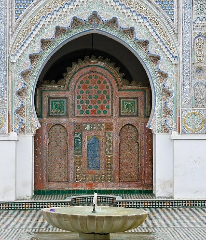 Elaborate mosaic arch with historical influences, featuring intricate patterns above a stone fountain.