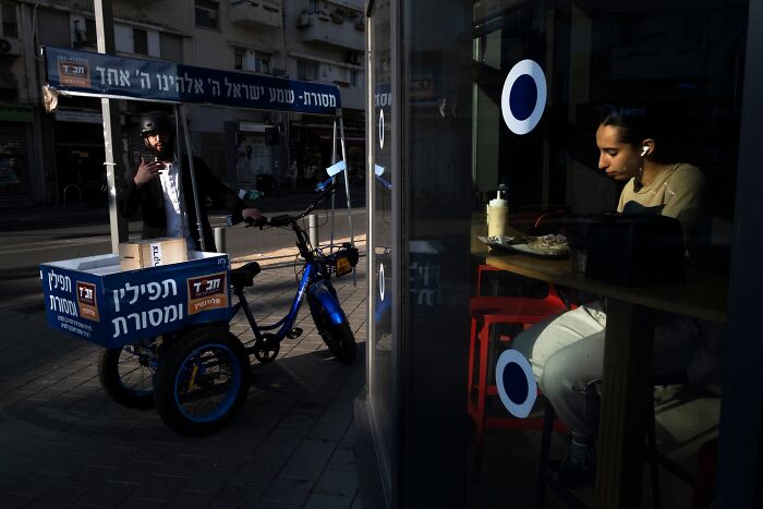 Street scene in Israel with a man on a bicycle and a woman sitting in a café, capturing everyday life.