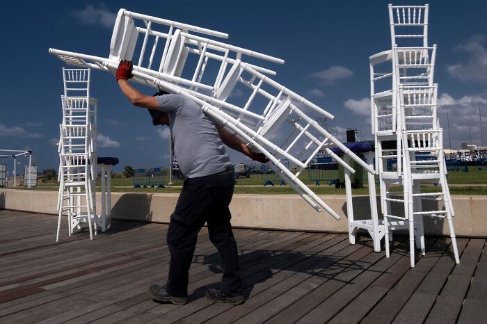 A man carries stacked white chairs outdoors in Israel.