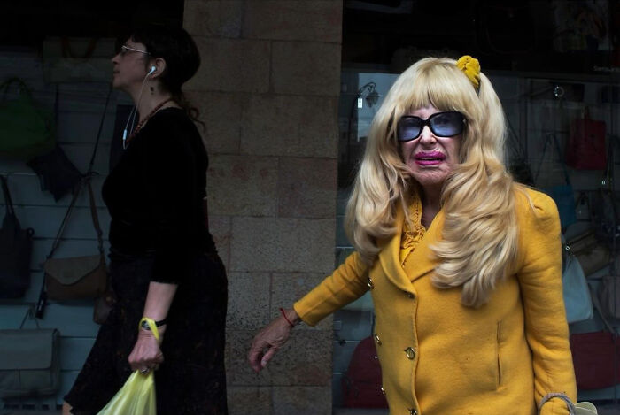 Two women on an Israeli street; one in a yellow outfit, the other walking by with earphones.