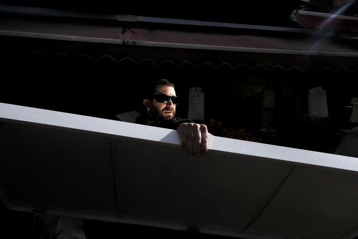 Man in sunglasses adjusting a canopy in harsh sunlight, captured in Israel street photography.