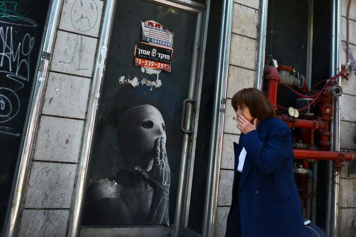 A woman reacts to street art depicting a masked figure on a door in Israel.