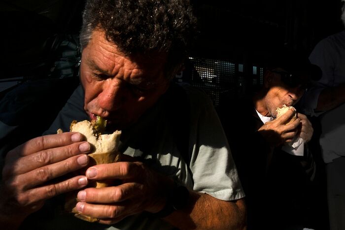 Man eating a sandwich in a dimly lit street setting in Israel, captured by Ilan Ben Yehuda.