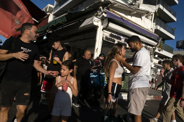 Street scene in Israel with people interacting, captured in a candid moment by Ilan Ben Yehuda.