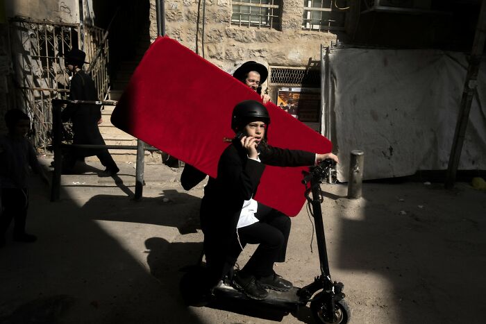 Street scene in Israel with a person on a scooter carrying a red item, photographed by Ilan Ben Yehuda.