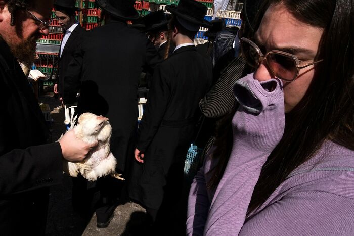 Street scene in Israel featuring two individuals, one holding a chicken and the other covering their face with a sleeve.