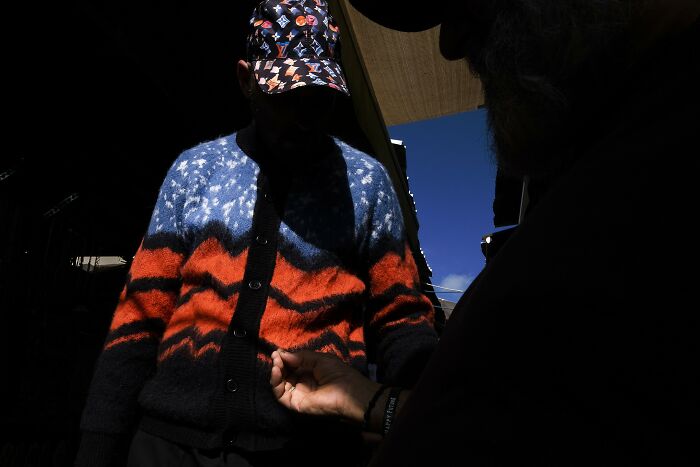 Street fashion in Israel captured in intense shadow and light. A person wearing a vibrant sweater and patterned cap.