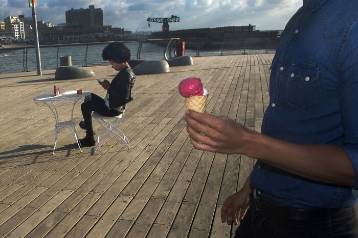 Man holding ice cream on a boardwalk, another person sitting at a table in Israel.