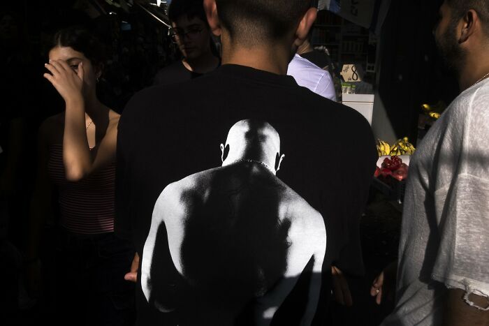 Street scene in Israel featuring people with one wearing a shirt displaying a monochrome muscular silhouette.