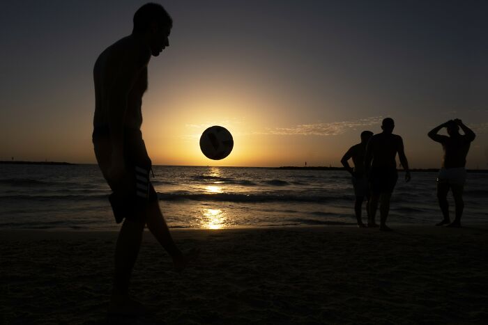 Silhouetted beachgoers playing soccer at sunset in Israel, captured by Ilan Ben Yehuda.