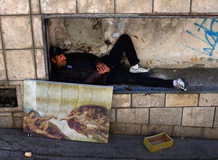 Street scene in Israel: a man resting in a recess with a replica of Michelangelo's Creation of Adam beside him.