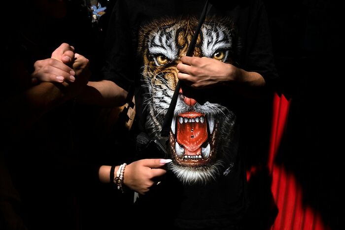 Street photo by Ilan Ben Yehuda of a person wearing a shirt with a roaring tiger design, holding hands with another person.