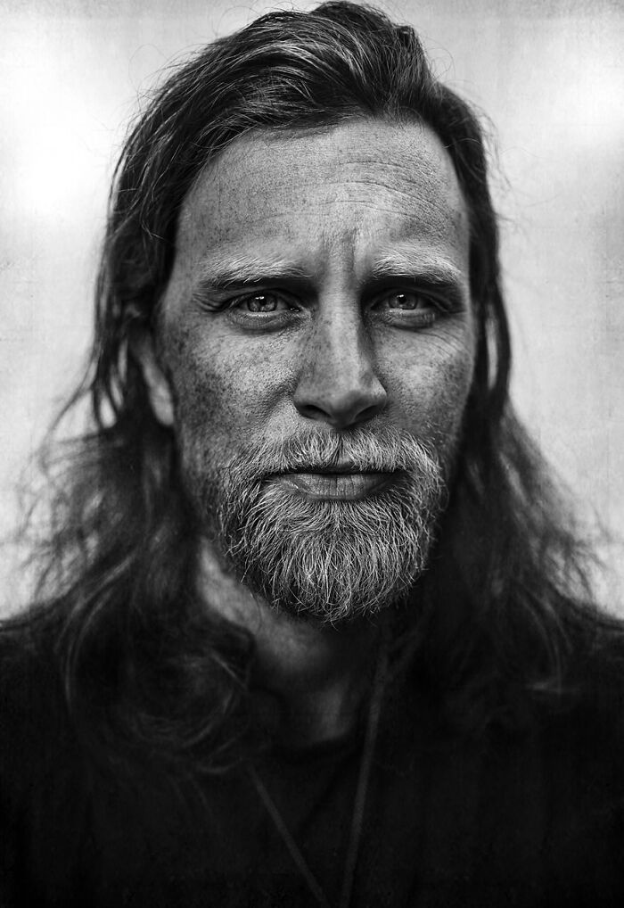 Soulful black and white portrait by Lee Jeffries, featuring a rugged man with long hair and a beard.