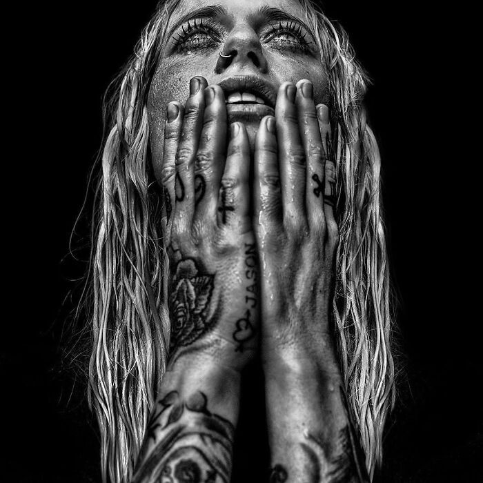 Tattoos on hands of a person looking up, captured in a soulful portrait by Lee Jeffries.