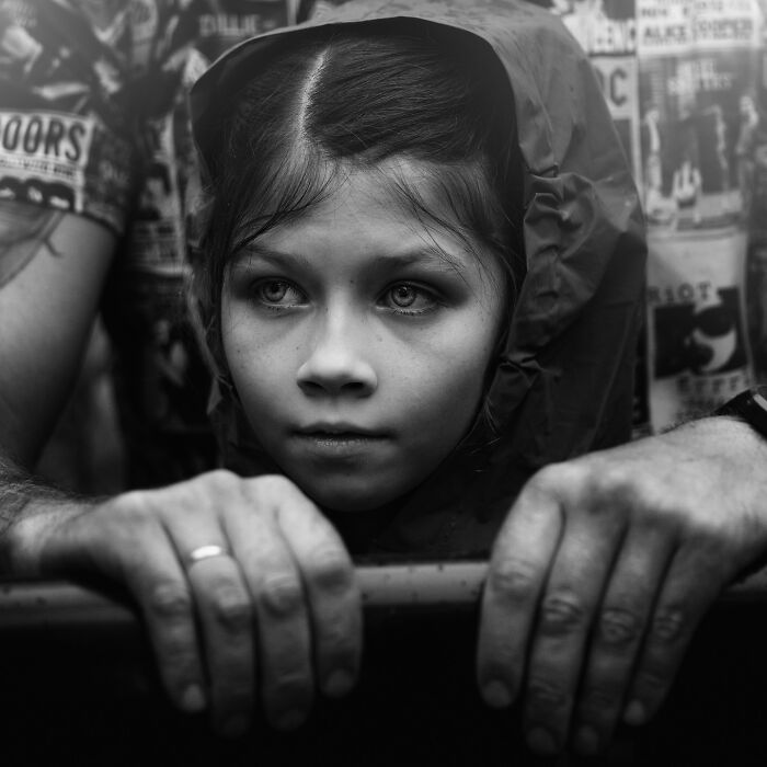 Young girl in a hooded jacket, gazes intently, framed by adult hands, captured in Lee Jeffries' soulful portrait.