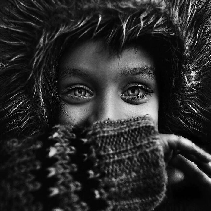 Black and white Lee Jeffries portrait of a person in a hood, captivating eyes peering over a knit sweater.