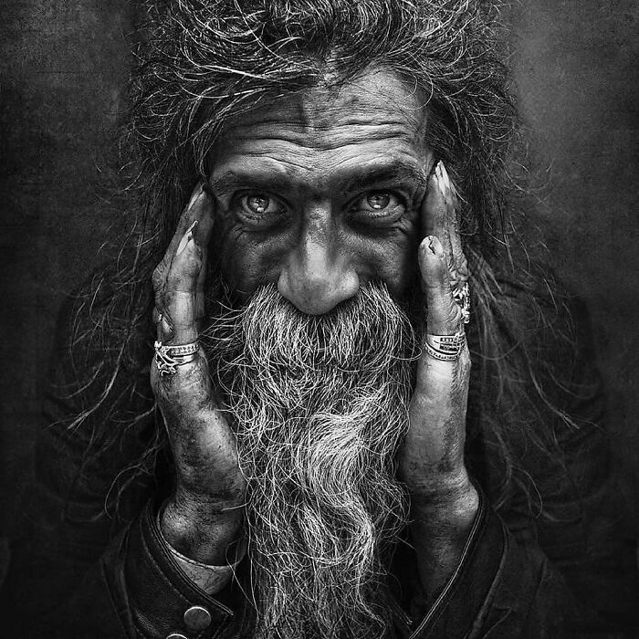 Soulful portrait of bearded man by Lee Jeffries, hands framed on his face, intense gaze into the camera.