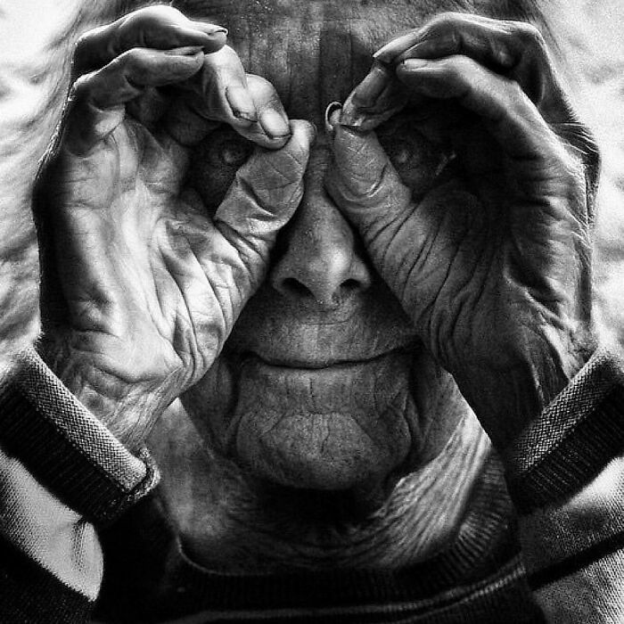 A soulful portrait by Lee Jeffries of an elderly person playfully forming glasses with their hands.