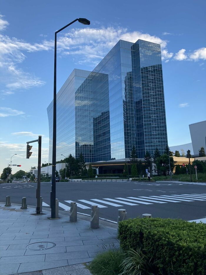 Futuristic glass building under blue sky, appearing like a computer render with sharp angles and reflective surfaces.