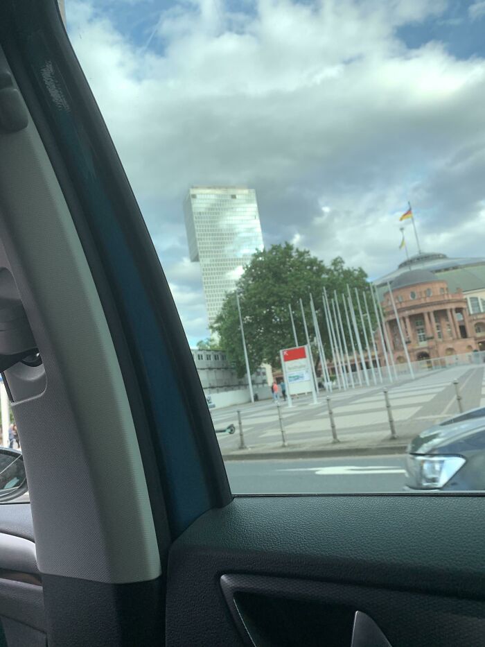 City view from a car window with a tall building against a cloudy sky, resembling a bad render.