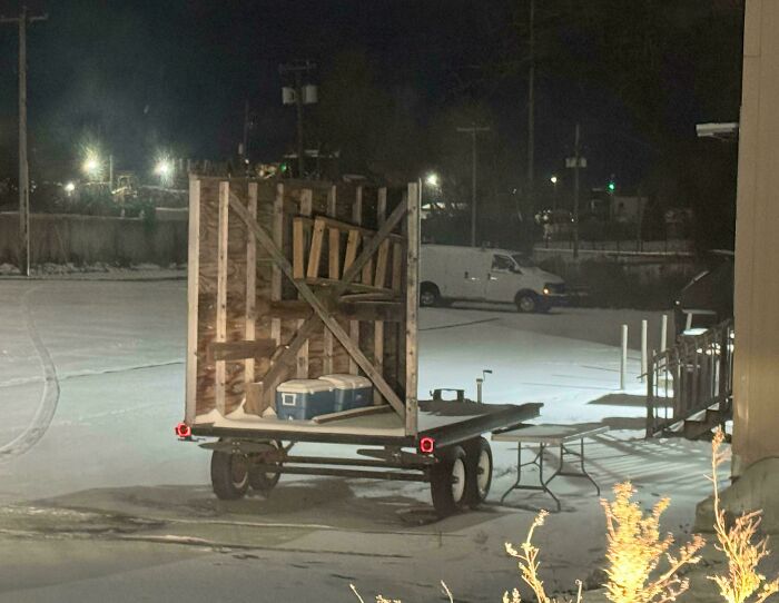 Trailer with wooden crates and a cooler in snowy parking lot at night; appears like a bad render.