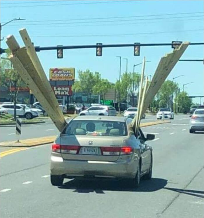 Car carrying oversized wooden planks awkwardly protruding through windows, driving down a busy street.