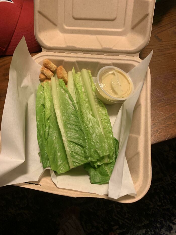 Unhinged food: Takeout box with lettuce leaves, croutons, and sauce cup.