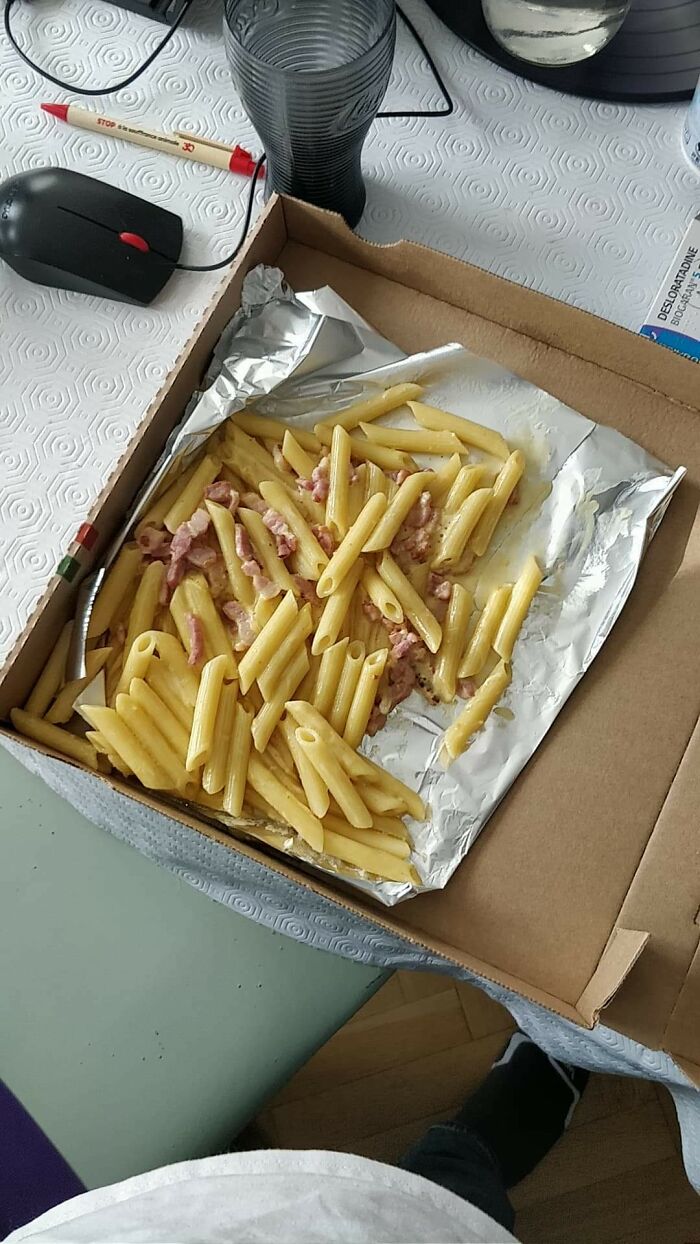 Unhinged foods: Penne pasta with bacon in a pizza box on a tabletop setting.