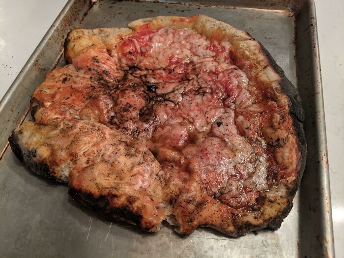 Unhinged foods: overcooked, distorted pizza on baking tray.