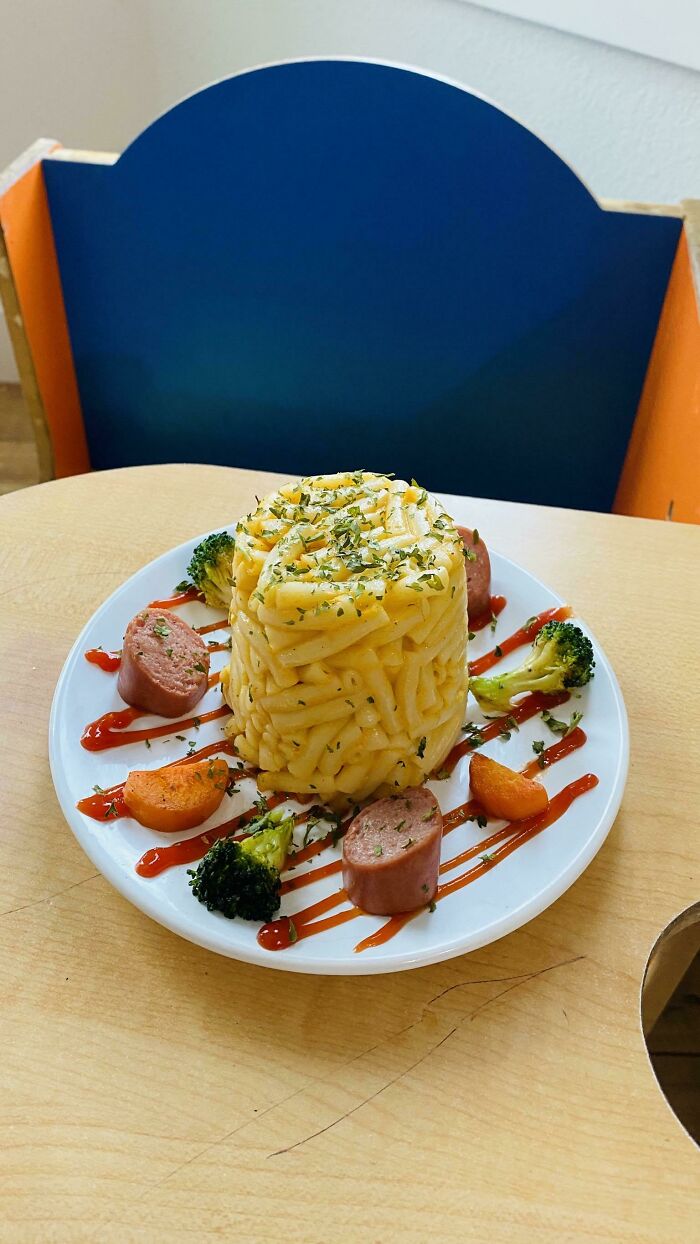 Unhinged food creation featuring a towering pasta stack with sausages, broccoli, and sauce drizzles on a plate.